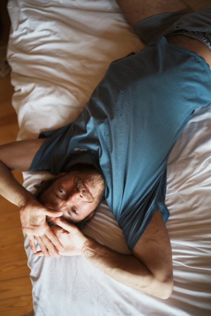 Photo by Katharina Roehler a man laying on top of a bed next to a wooden floor