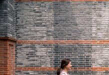 일상 속 걷기, 건강을 지키는 가장 손쉬운 비결 A woman walks along a brick wall.