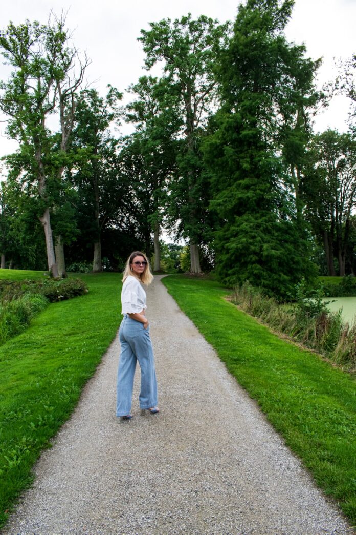 Photo by Zuzana Ruttkay woman in white long sleeve shirt and blue denim jeans standing on gray asphalt road during